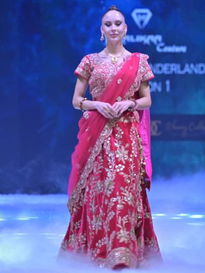 The model walks the runway in the red and gold embroidered lehenga, surrounded by a dramatic mist. This piece is designed to be as powerful as it is beautiful.