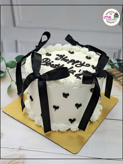 A chic black and white birthday cake. The white buttercream is decorated with little black hearts and tied with elegant black ribbons for a modern and stylish look.