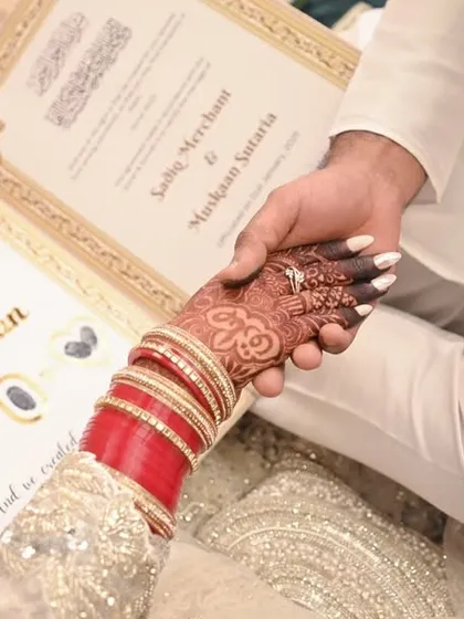 The joining of hands over the Nikahnama, symbolizing their union. This is a powerful detail shot that signifies the official start of their marriage, rich with cultural importance.