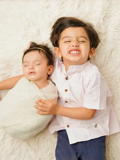 A big brother's cheesy grin as he holds his sleeping newborn sibling. This photo perfectly captures the mix of pride and playfulness in a new big brother.