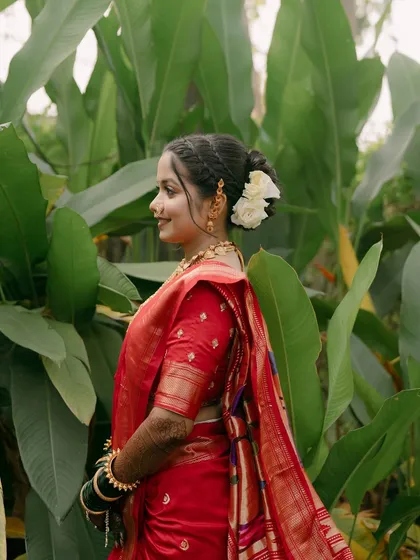 A beautiful bride in a red Paithani saree, her hair adorned with a white flower.