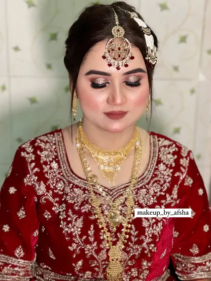 A classic bridal portrait. The bride is wearing a beautiful red velvet outfit with gold jewellery. The makeup is glamorous, with glittery eyes and a soft brown lip.