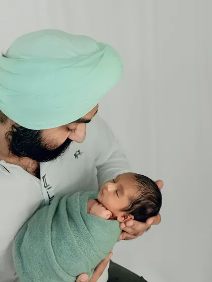 A father holds his newborn, wrapped in a soft green swaddle that complements his turban. The image is a beautiful blend of modern fatherhood and cultural identity.