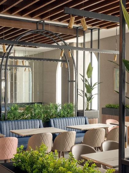 The dining area at Haldiram's features a furniture palette of beige, deep blue, and blush pink, adding vibrancy to the space. Metal arches with integrated planters serve as dividers, creating semi-private seating zones.