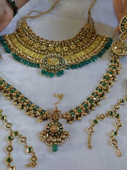 A complete bridal jewellery set laid out. This shows the full rental package, including the choker, long necklace, hathphool, and matha patti, all in a matching green Kundan design.