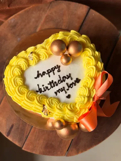 A sunny yellow heart-shaped cake for him, decorated with golden spheres and an orange ribbon.