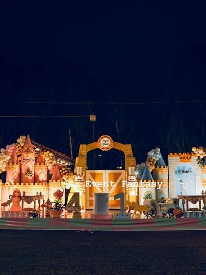 A wide shot of the royal celebration stage for twins Smyra and Dishir. The setup features two distinct castle areas, one pink and one blue, united by a central barn door entrance.