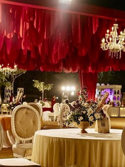An opulent reception space with a ceiling of hanging red fabric petals and numerous crystal chandeliers, creating a luxurious and romantic atmosphere.