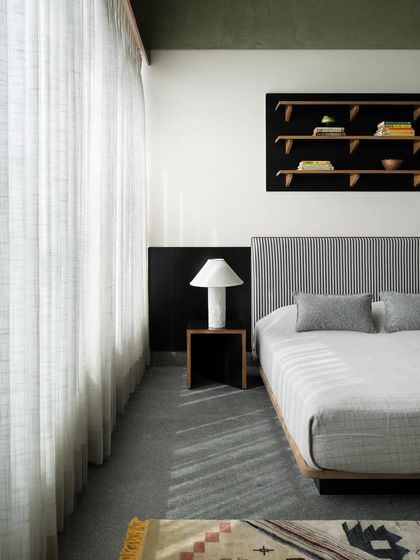 A son's bedroom with a custom striped headboard and a floating black shelf unit. The design uses strong graphic elements like stripes and solid black to create a modern and youthful yet sophisticated space.