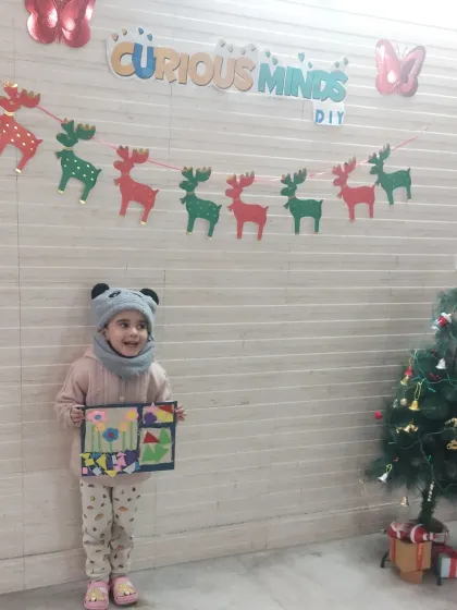 A happy student stands next to the Christmas tree, holding her completed artwork. Our festive workshops are full of joy and opportunities to create holiday-themed masterpieces.