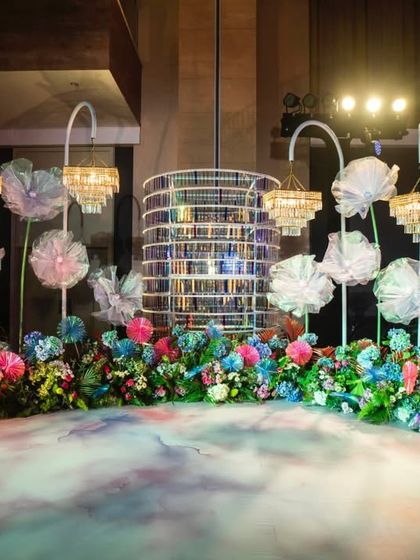 A whimsical photo booth or lounge area at the Sangeet, featuring oversized, translucent flowers, elegant crystal chandeliers, and a custom-painted floor. It’s a perfect blend of fantasy and modern design.