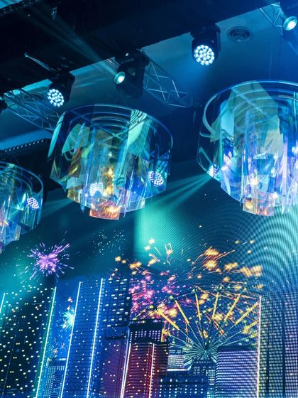 A detailed shot of the custom-made iridescent chandeliers hanging over the stage. These fixtures refract light in multiple colors, adding to the glamorous and futuristic theme of the event.