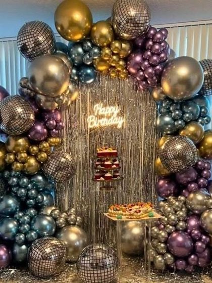 A retro disco theme perfect for an adult birthday party. This decoration is built around a silver fringe curtain and an arch of chrome and metallic balloons, with disco balls scattered throughout for a fun, party vibe.