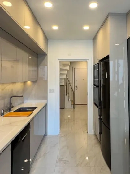 A sleek galley kitchen in Neeti Bagh with high-gloss, handleless cabinets. The design maximizes storage and workspace in a narrow layout, featuring recessed lighting and a marble-effect backsplash.