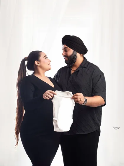 A sweet moment captured as the couple holds up a baby onesie. This is a lovely way to announce their excitement, and the simple black outfits keep the focus on the moment.