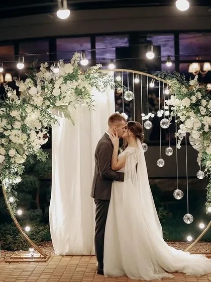 A couple shares a kiss in front of a beautifully lit floral arch, a perfect photo moment I can help create for you.
