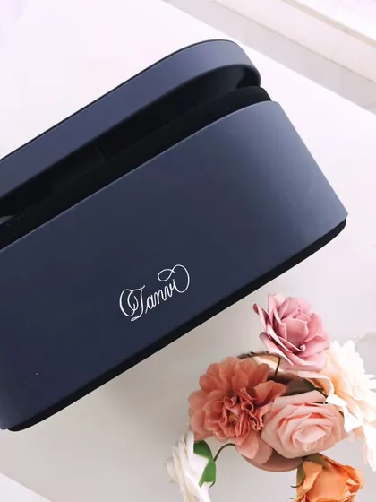 A top down view of the personalized Dyson case, surrounded by delicate flowers. The simple, elegant script of the name 'Tanvi' makes this a truly special and luxurious self-care accessory.
