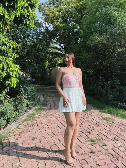 A full-length view of the pink corset and white skort outfit in a park setting.