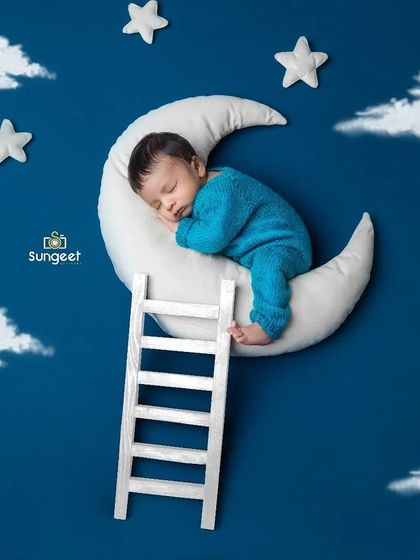 To the moon and back. This dreamy newborn setup features a baby sleeping on a crescent moon against a deep blue, starry sky, complete with a tiny ladder to climb.