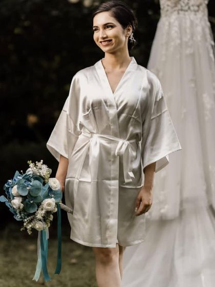 A bridesmaid getting ready, holding a blue and white bouquet I designed for the bridal party. The wedding dress hanging in the background shows how we coordinate all the floral elements for the big day.