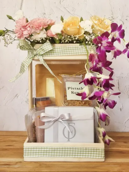 A stunning Mother's Day hamper featuring a wooden box overflowing with fresh flowers like orchids and carnations, alongside our gourmet treats.