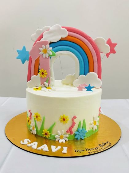 This rainbow-themed cake is all about childhood joy. It features a big, bright rainbow topper, colorful stars, and little flowers, perfect for a vibrant first birthday party.