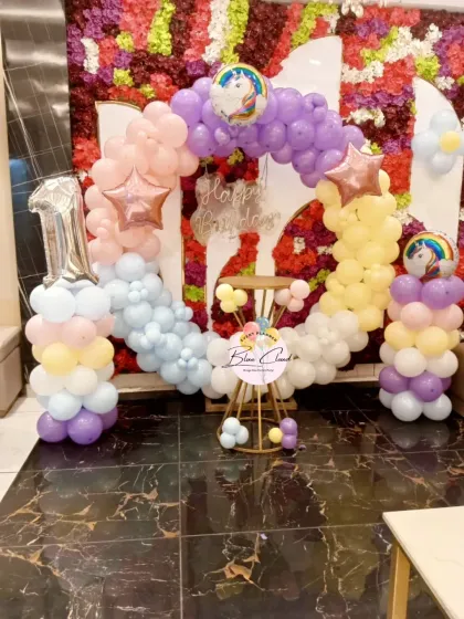 A pastel-colored unicorn theme for a first birthday, featuring a balloon arch against a floral wall.