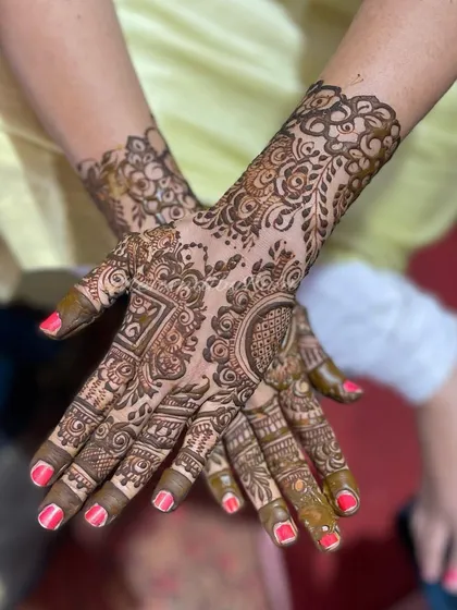 A beautiful, full-coverage design with a mix of geometric and circular patterns. The bright pink nails add a lovely pop of color against the henna.
