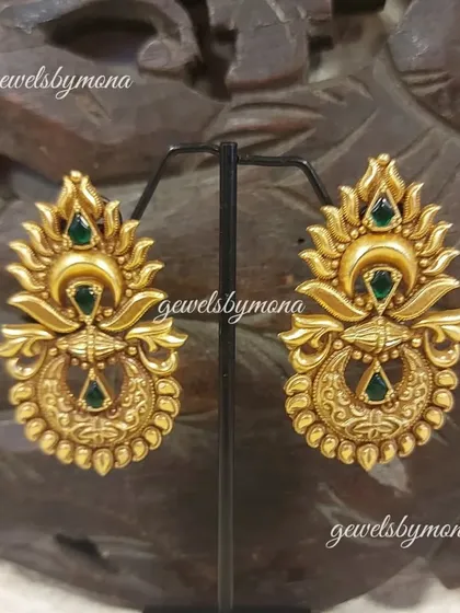 These ornate Dakshinaya earrings showcase a crescent moon design with intricate carvings and green stone accents, reflecting the divine motifs found in traditional temple jewellery.