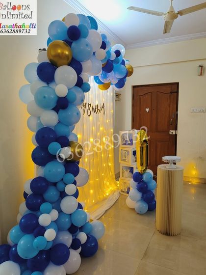 A blue, white, and gold balloon arch with a light curtain, creating a beautiful and celebratory corner for a first birthday at home.