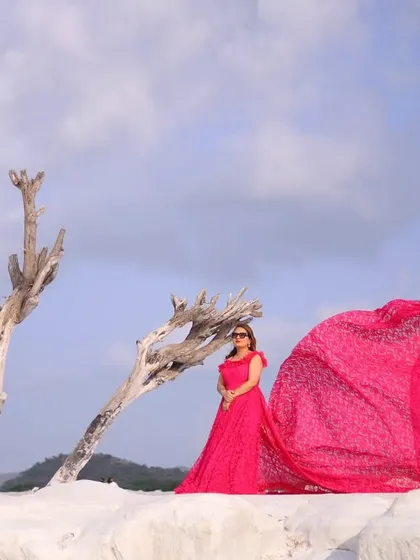 A high-fashion, dramatic pre-wedding portrait. The vibrant pink gown flowing in the wind against a stark, minimalist landscape creates a visually stunning and unforgettable shot.