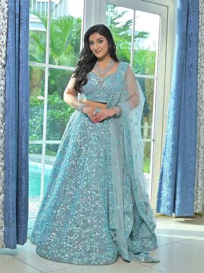 A full-length portrait of the model in the ice blue lehenga, showing its elegant silhouette against a poolside backdrop.