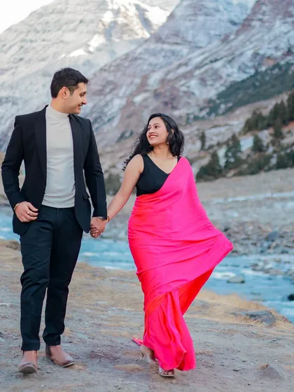 A couple walks hand-in-hand along a riverbank in Himachal, the bride's vibrant pink saree a beautiful contrast to the landscape.