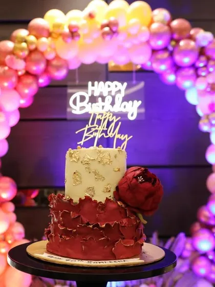 A stunning two-tiered birthday cake with a red floral design, perfectly complementing the colorful balloon arch backdrop.