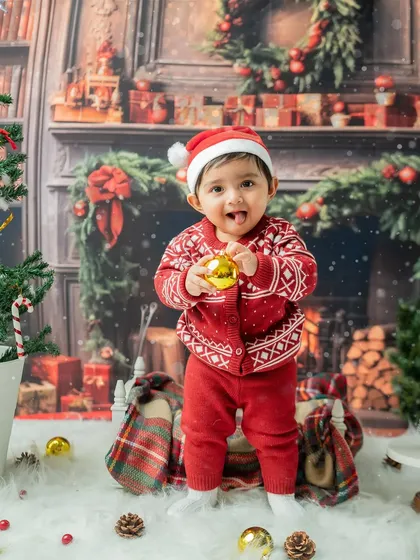 A playful toddler standing and holding a golden bauble. The joy and excitement of the holidays are clear on his face.