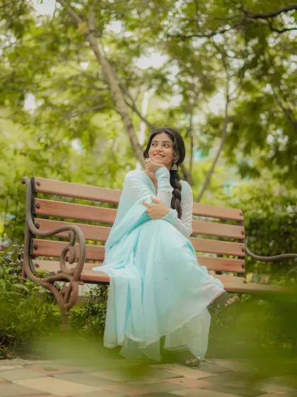 A serene and graceful portrait in a park setting. The natural environment complements the simple elegance of the light blue ethnic suit.