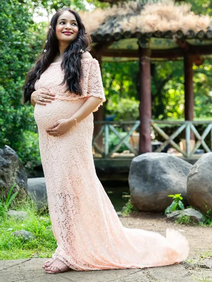Elegance in the garden. This expecting mother looks serene and beautiful in a full-length peach lace gown, cradling her baby bump.