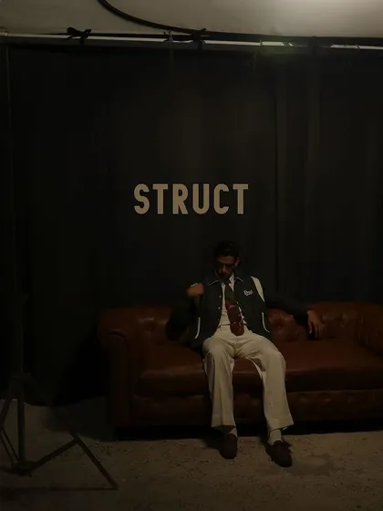 A candid moment on the set of the Struct AW'24 shoot, with the model relaxing on the couch against the branded backdrop.