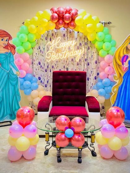 A princess-themed birthday setup with a throne for the birthday girl, flanked by cutouts of Ariel and Rapunzel.