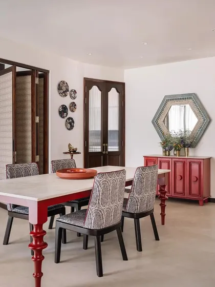 The dining room features a unique table with lacquered red legs, paired with a distressed hexagonal mirror and a collection of ceramic plates.