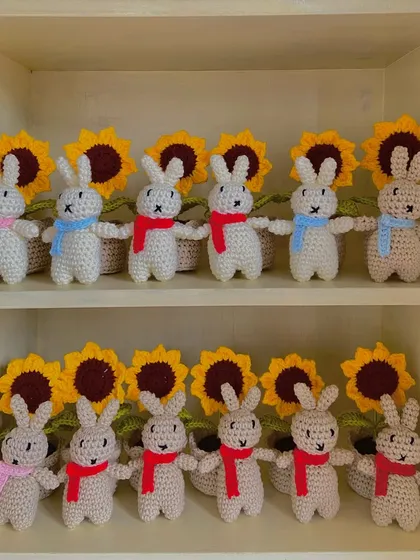 A cute display of my amigurumi bunnies lined up in front of potted sunflowers on my shelf.