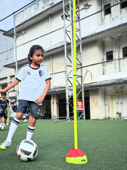 A young girl practices her dribbling skills around a training pole, demonstrating focus and determination during one of our skill-based sessions.