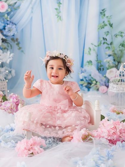 A happy wave from the floral wonderland. This baby girl's joyful expression and wave make for a delightful and engaging photograph.