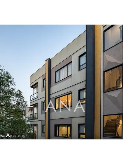 Another view of the side facade of the Yellow Line Apartment, highlighting the rhythmic placement of windows and the contrast between the beige, grey, and yellow elements.