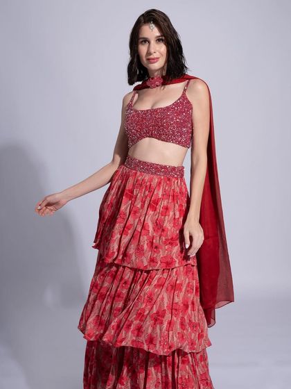 A festive look featuring a red floral lehenga. The makeup is fresh and pretty, with a simple maang tikka and a pop of color on the lips.
