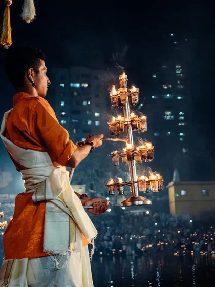 A powerful shot of a priest with the ceremonial lamp, the light illuminating his face against the dark water and city lights.