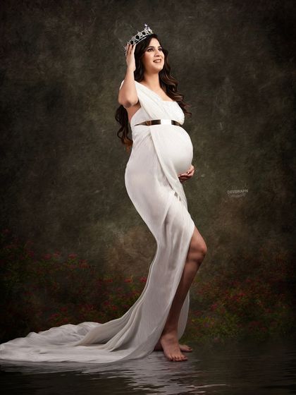 A regal and confident portrait. The client wears a simple white gown and a crown, creating a powerful image of a queen awaiting her heir. The water reflection adds a touch of magic.