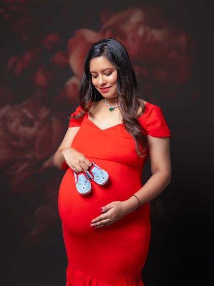 Anticipation in her eyes, love in her heart, and tiny shoes ready to take on the world. A beautiful moment in a striking red dress.