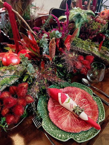 This detailed shot highlights the exotic textures within the table runner, including rambutan fruit and various types of red flowers and foliage, creating a visually fascinating display.