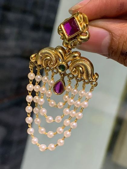 A closer look at the imitation gold-look earrings with cascading pearl drops. The intricate design and the vibrant ruby-colored stone make them look very luxurious.